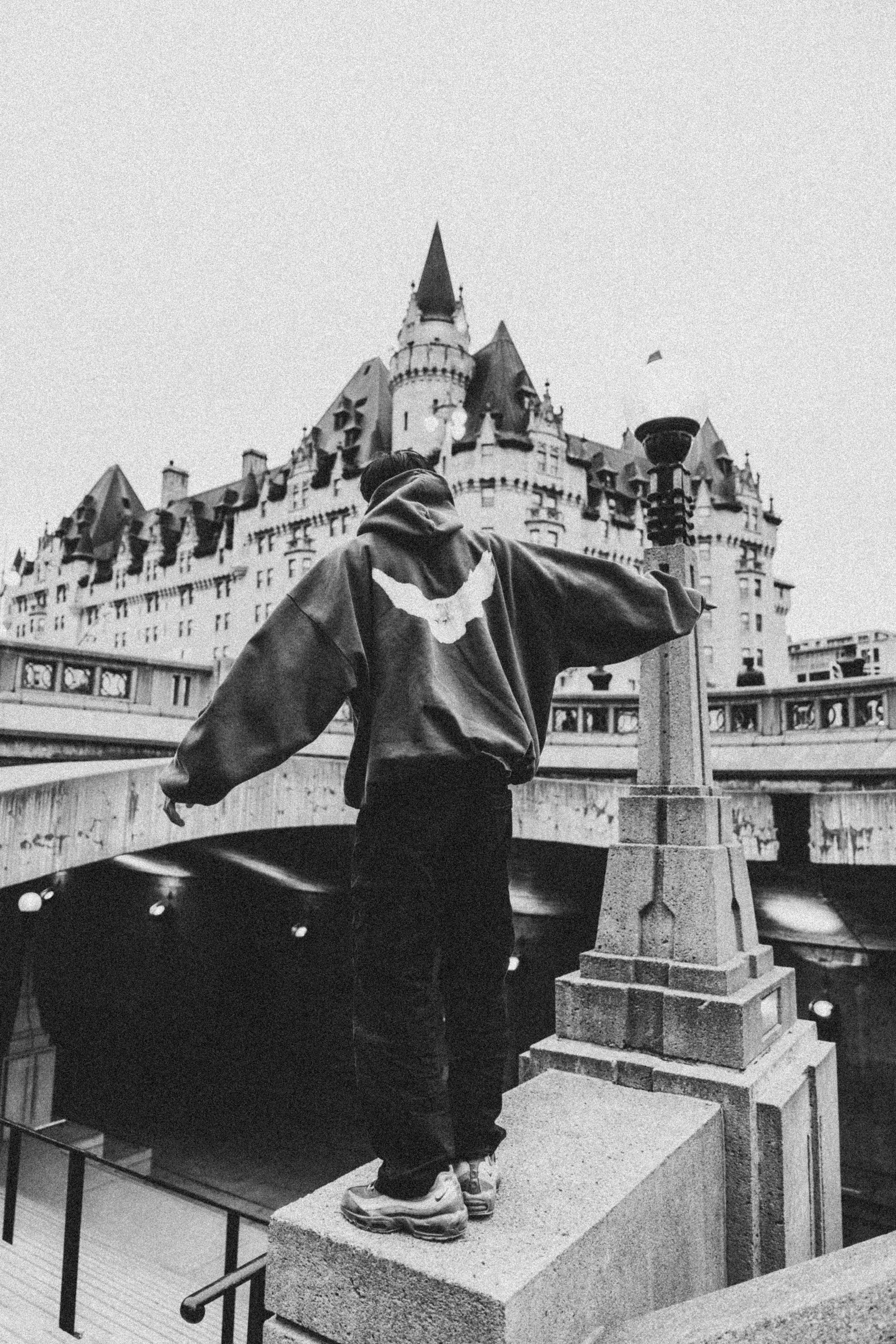 Person in a hoodie stands near iconic castle-like building, showcasing modern urban style.