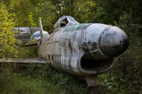 Free An old military jet resides abandoned in a lush, overgrown forest area. Stock Photo