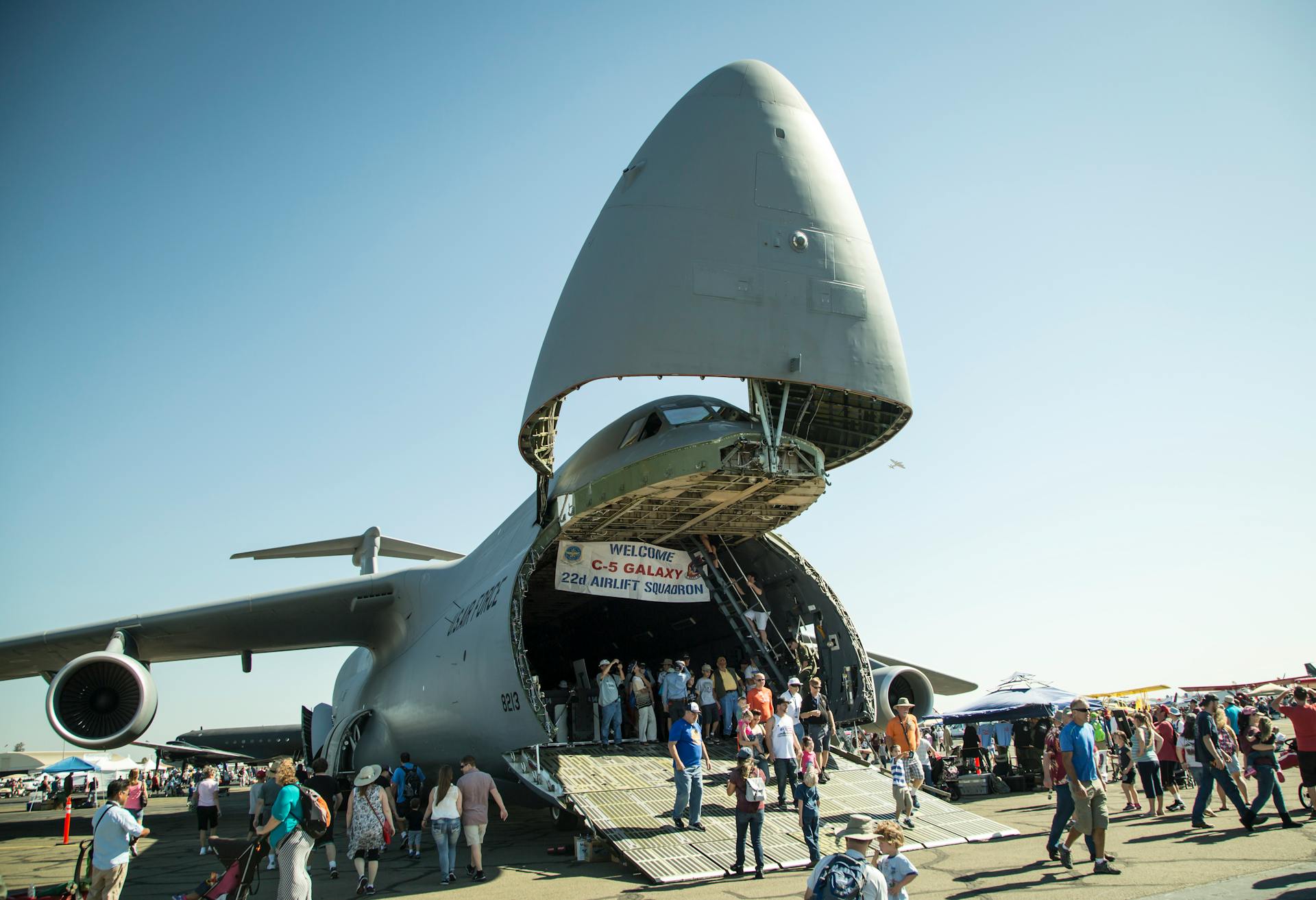 Crowd explores a C-5 Galaxy aircraft at an airshow. Clear sky and vibrant atmosphere.