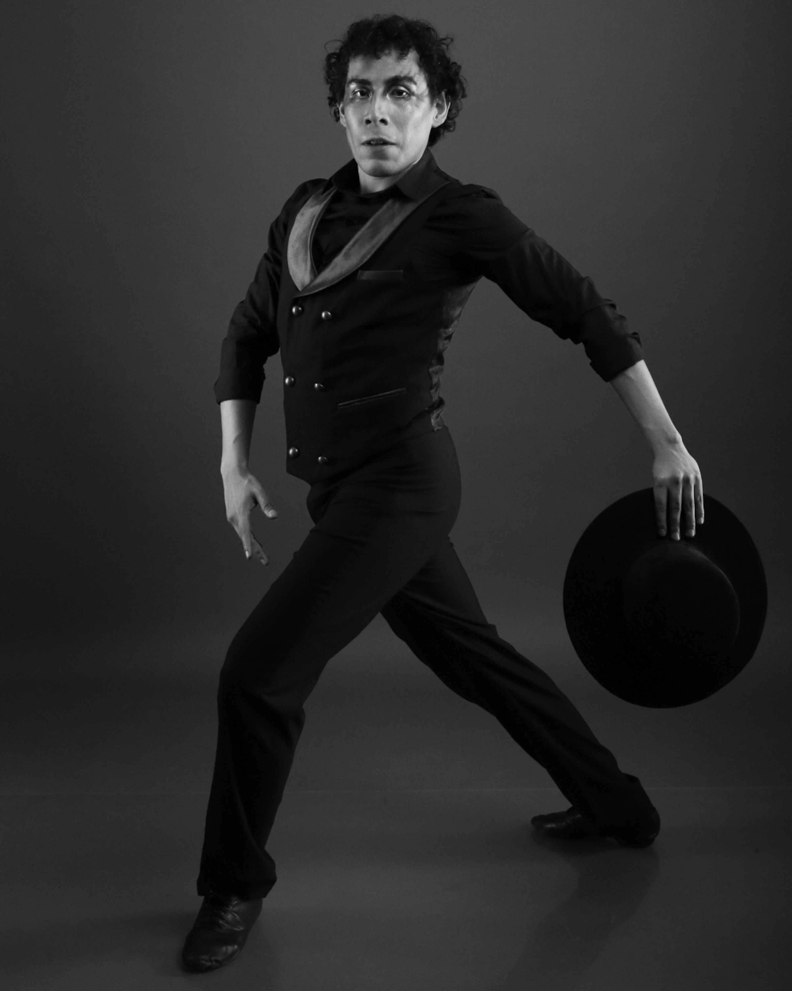 Expressive flamenco dancer in dramatic pose, holding hat, in black and white.