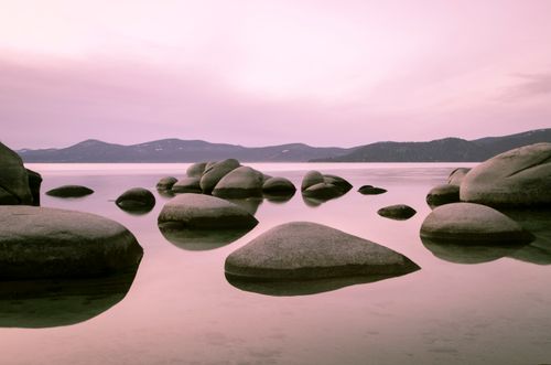 Free Tranquil pink-hued sunset over Lake Tahoe with smooth rocks and distant mountains. Stock Photo