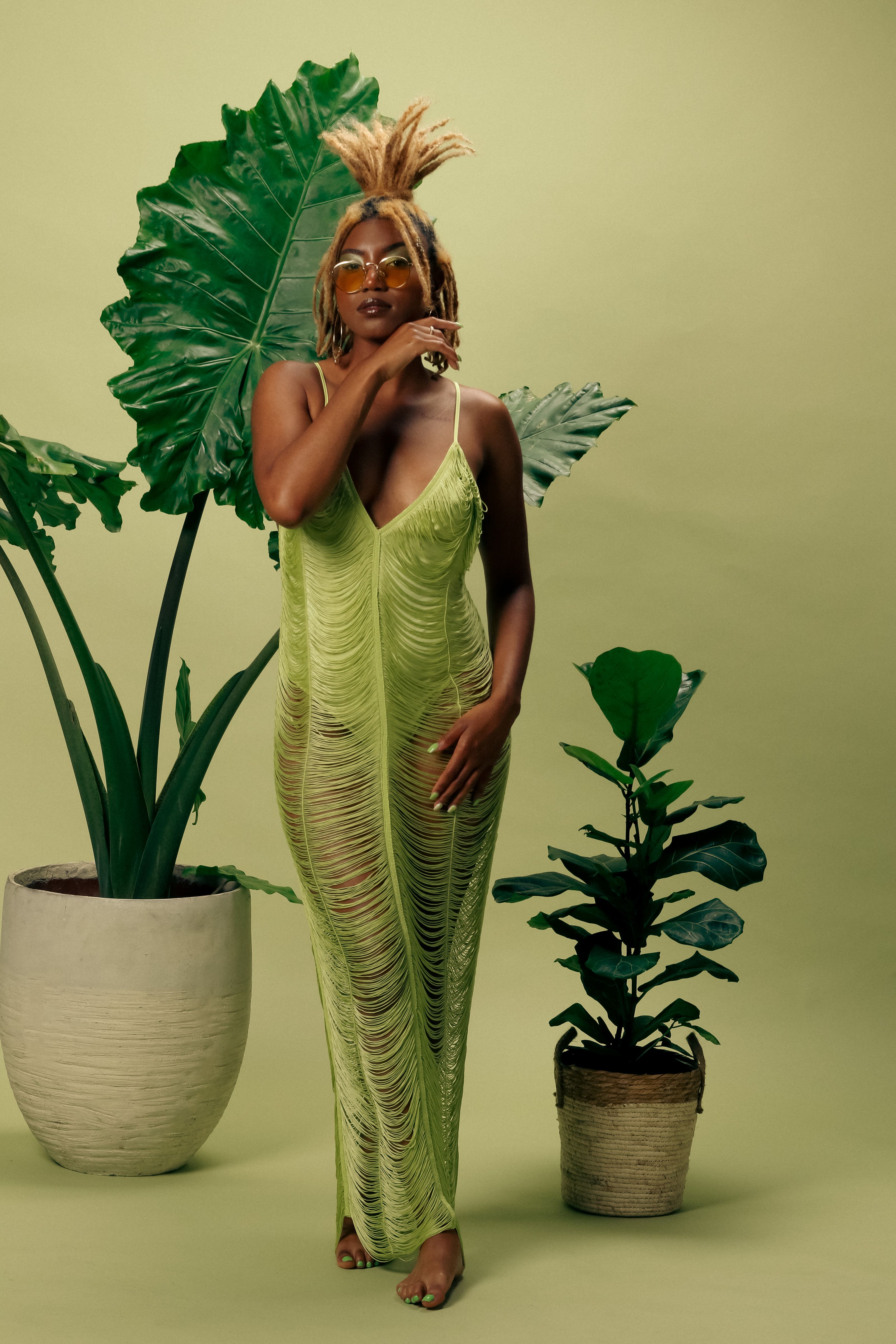 Mulher estilosa em um vestido verde posa com plantas tropicais indoors. Moda moderna.