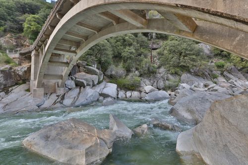 Free Concrete bridge spanning a rocky river with lush greenery in a natural setting. Stock Photo
