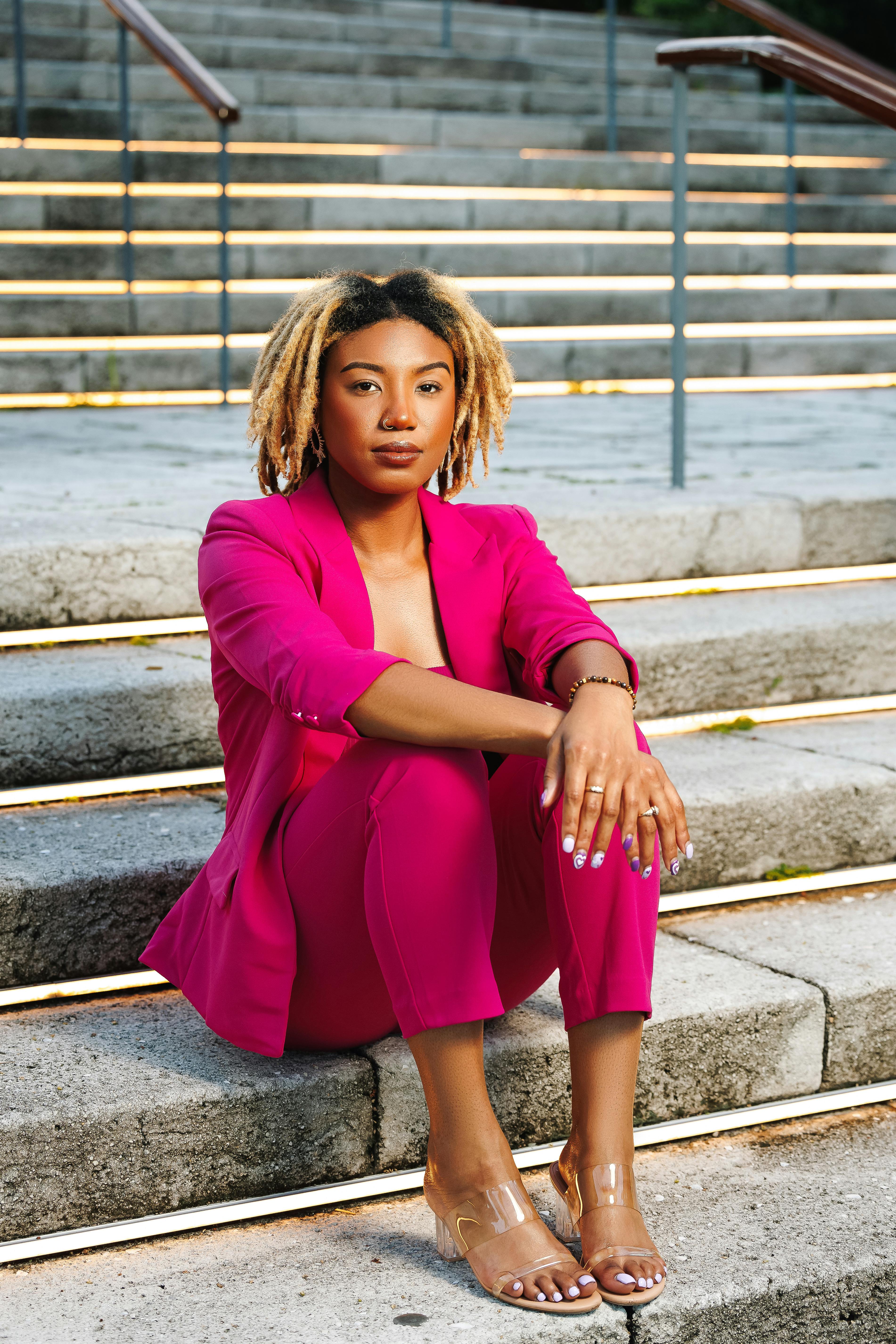 Stylish woman in pink suit poses confidently on outdoor steps.