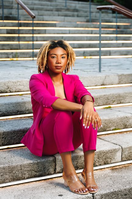 Stylish woman in pink suit poses confidently on outdoor steps.