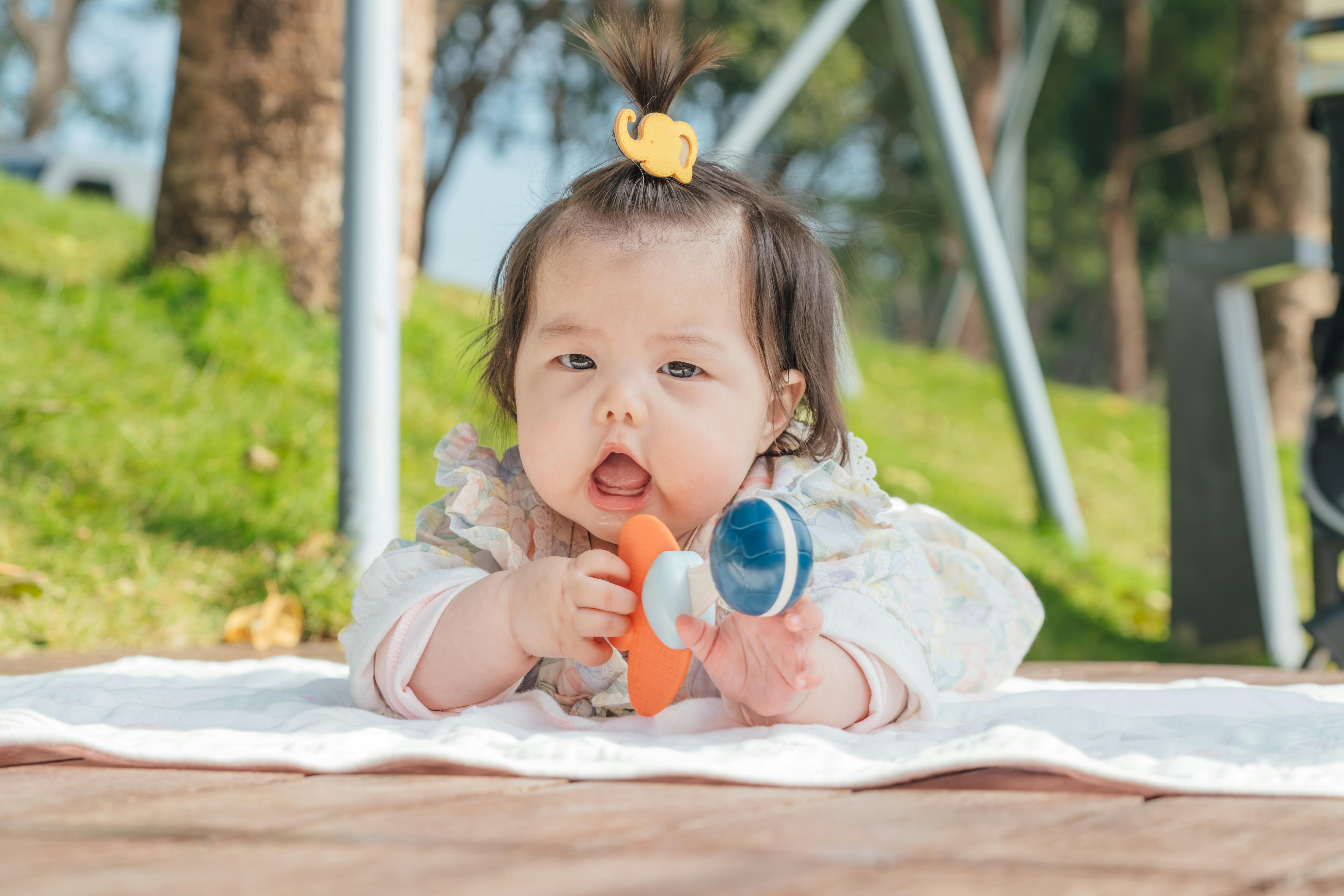 Cute Asian baby enjoying playtime on a blanket outdoors with a toy.