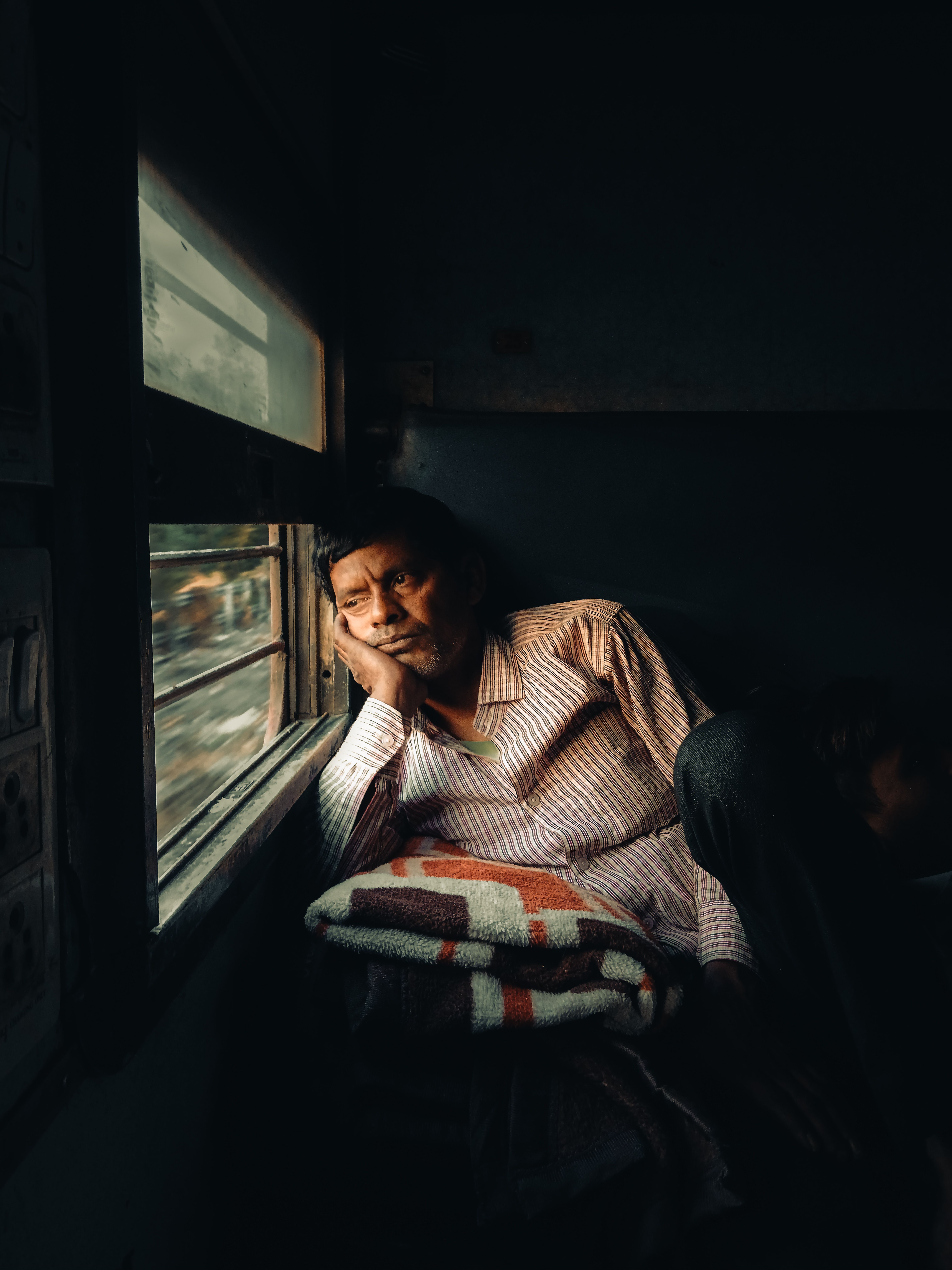 Elderly man in train, lost in thought, gazes out the window during daytime travel.