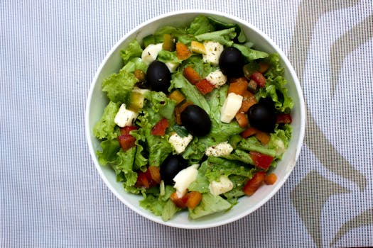 A vibrant bowl of fresh Greek salad featuring crisp lettuce, black olives, cheese, and diced vegetables.