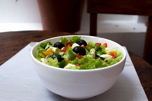 Delicious fresh salad with black olives, lettuce, and veggies in a white bowl indoors.