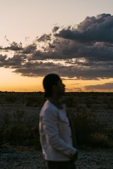 广阔的风景中，一个人面对戏剧性的日落，留下宁静的轮廓