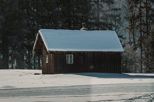 Rustic wooden cabin covered in snow, nestled in a peaceful forest setting.