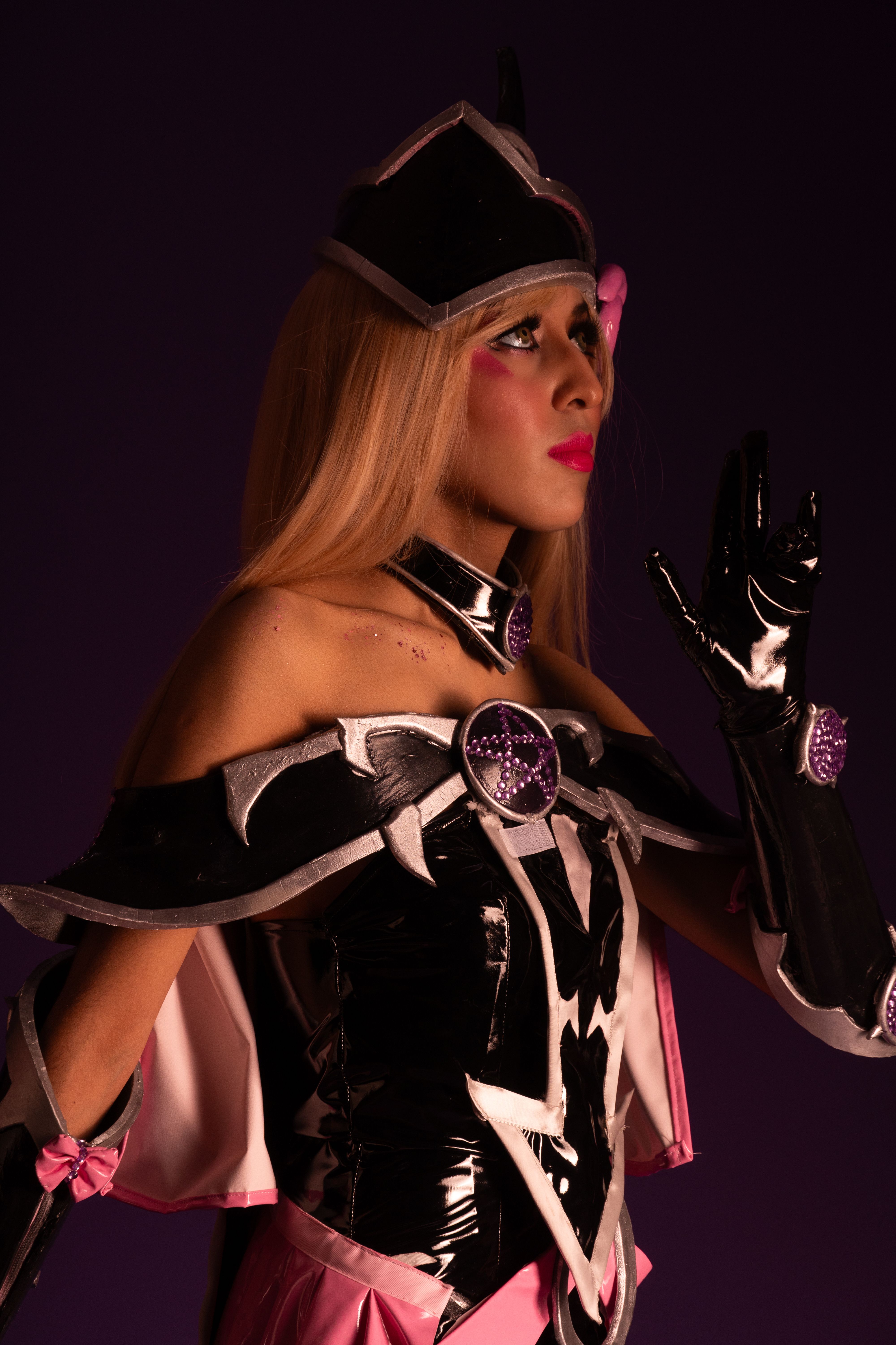 A cosplayer in colorful anime costume poses against a purple backdrop.