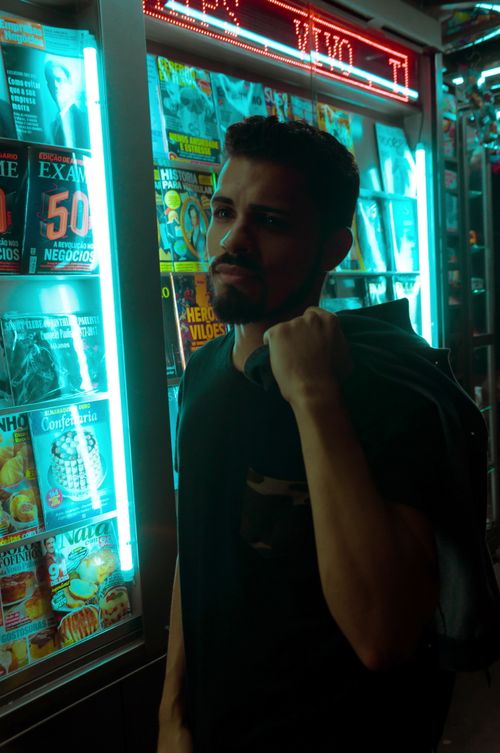 Free A fashionable man poses by a neon magazine stall in São Paulo's night. Stock Photo