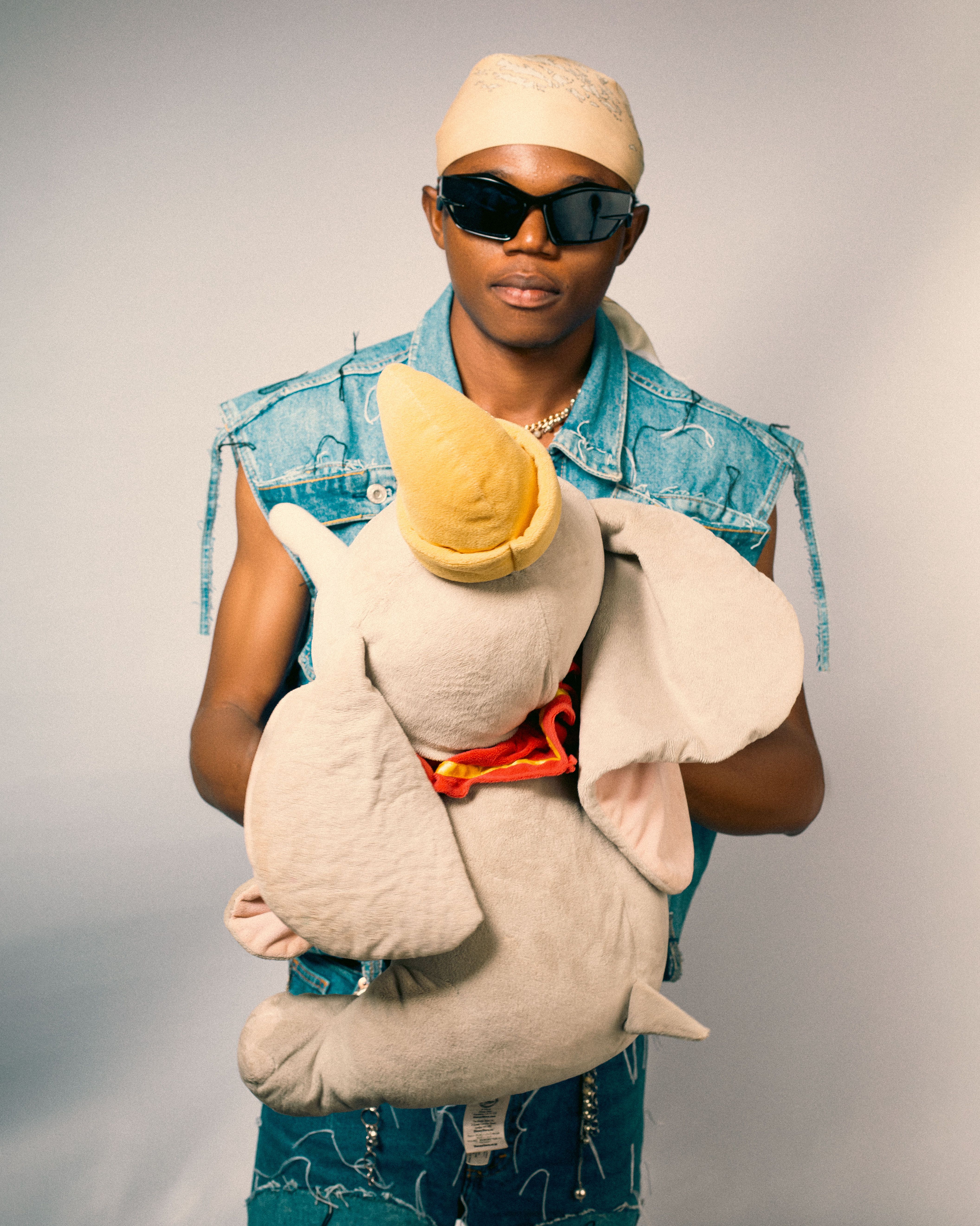 Fashionable young man in denim holding a large plush elephant toy; portrait photography.