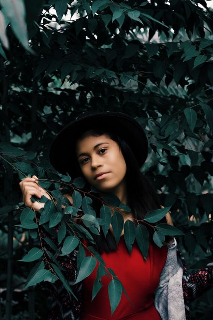 Elegant woman in red dress poses outdoors among leafy foliage, Rio Vermelho, MG.