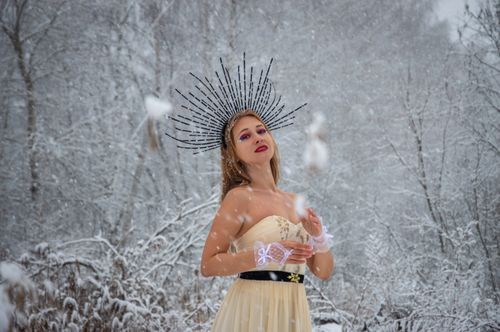 Free Woman in a snow-covered forest, wearing a unique crown and elegant dress, enjoying falling snow. Stock Photo