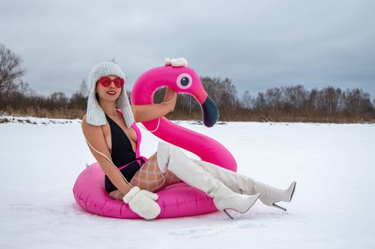 Woman in winter attire enjoys a pink flamingo float on a snowy day, contrasting vibes.