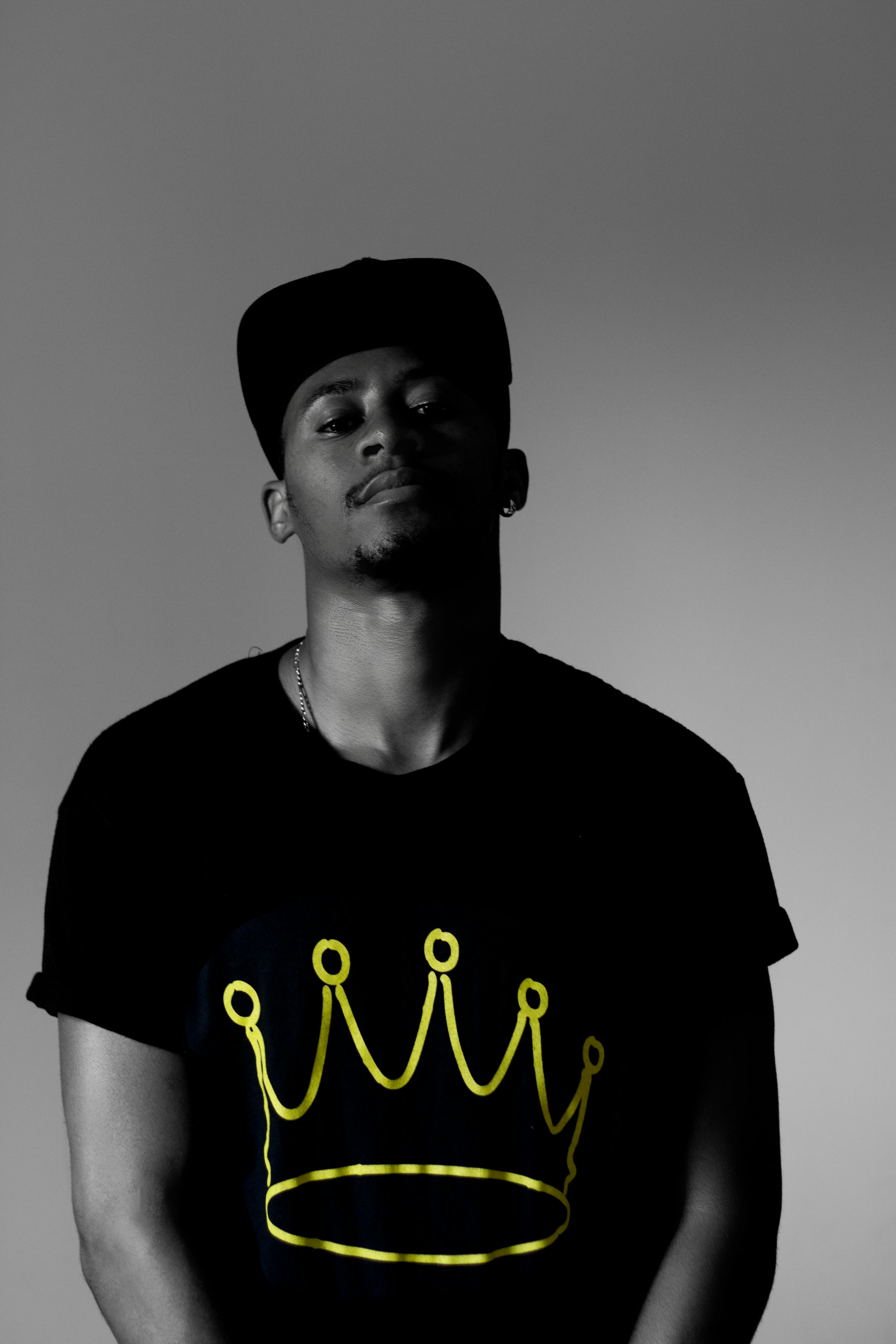 这是一张黑白肖像，画面中一名男子身穿印有皇冠图案的衬衫，整体色彩非常克制