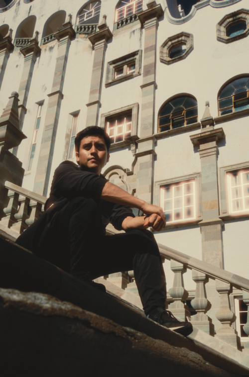 Free Man sitting on stairs in front of a historic building under clear skies. Stock Photo
