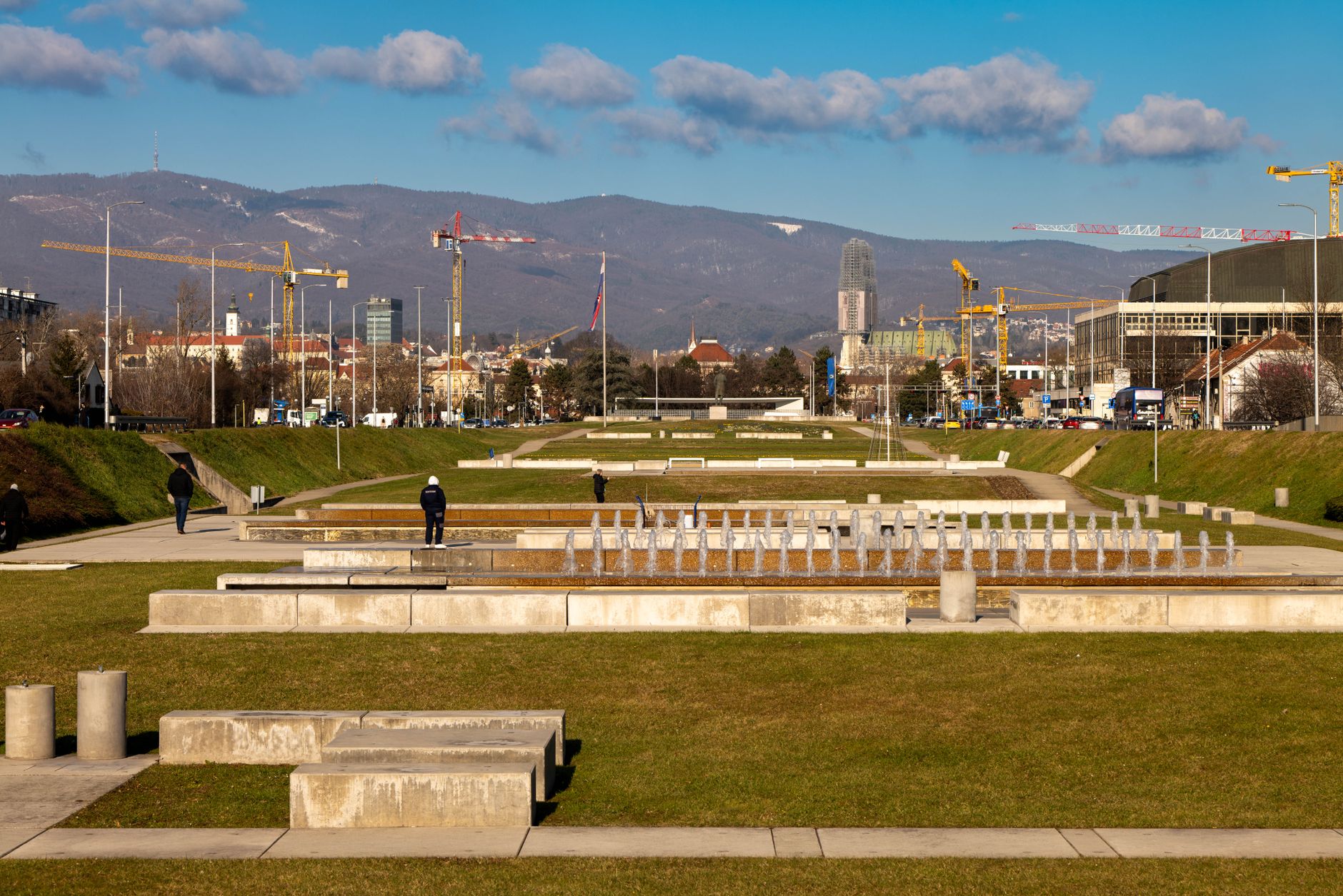 Vibrant scene of fountain park with city skyline and cranes, Zagreb, Croatia.