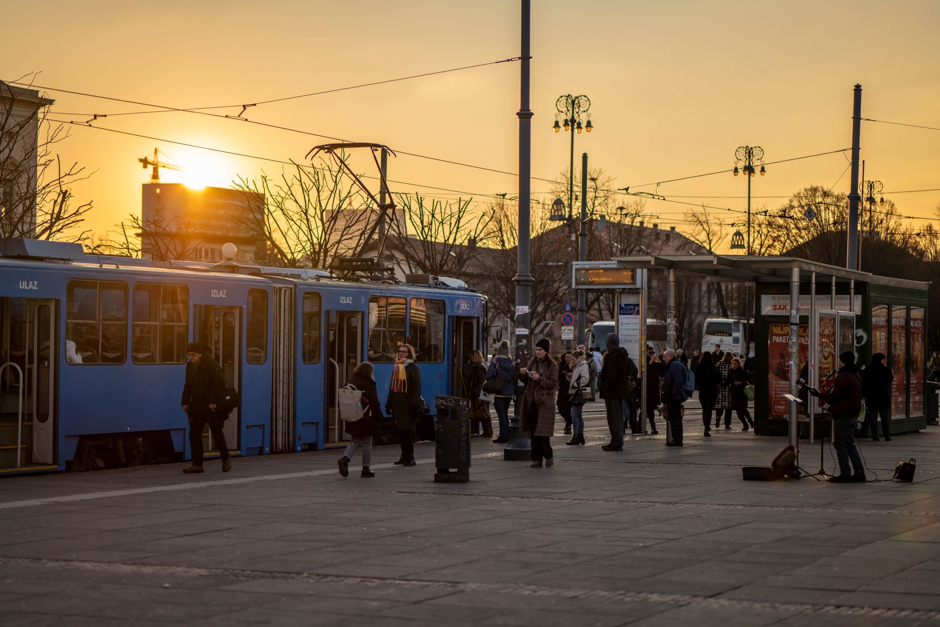 People boarding trams during sunset in Zagreb, creating a vibrant urban scene with warm tones.