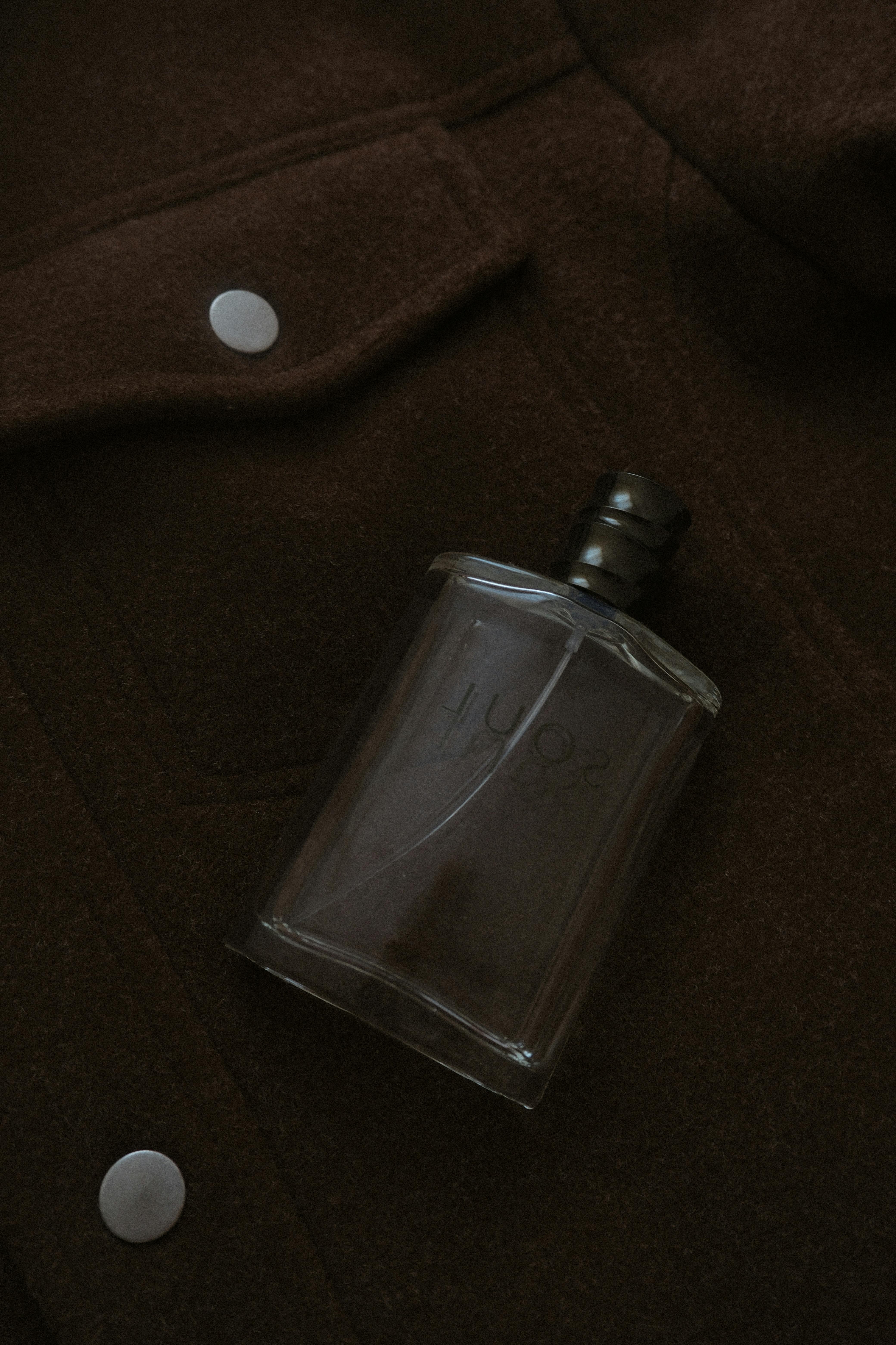 Stylish perfume bottle placed on dark brown woolen jacket, evoking sophistication.
