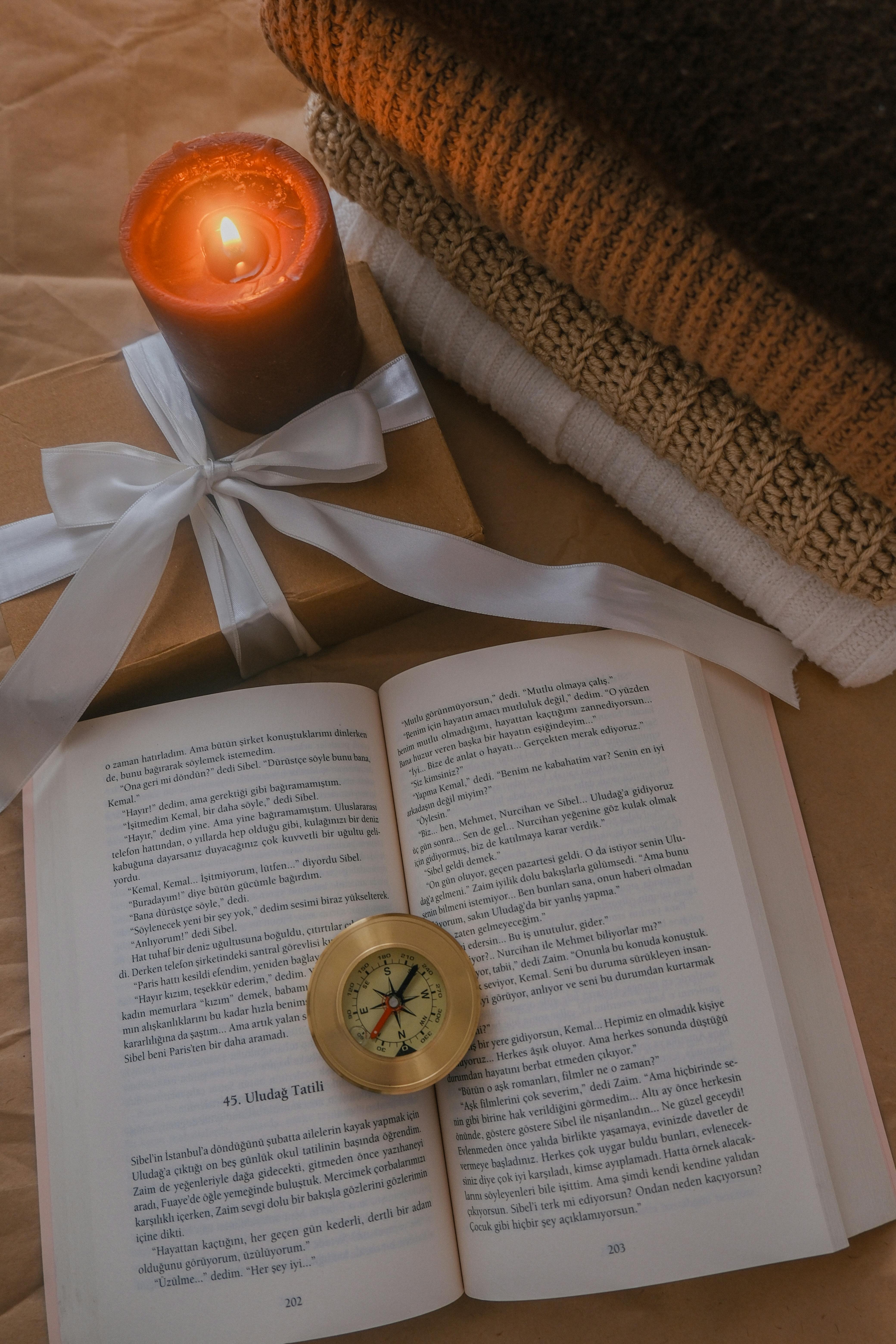 An inviting reading scene with a candle, book, compass, and cozy textiles.