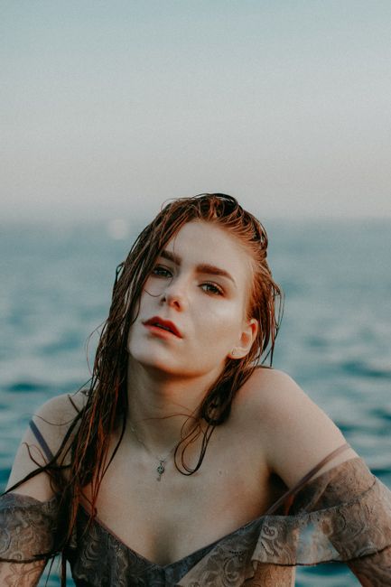 Elegant woman posing by the serene ocean, showcasing a fashionable style with natural beauty.