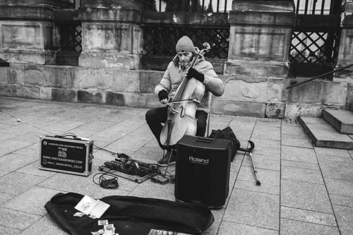 Free An adult street musician playing the cello in Krakow's historic streets, captured in black and white. Stock Photo