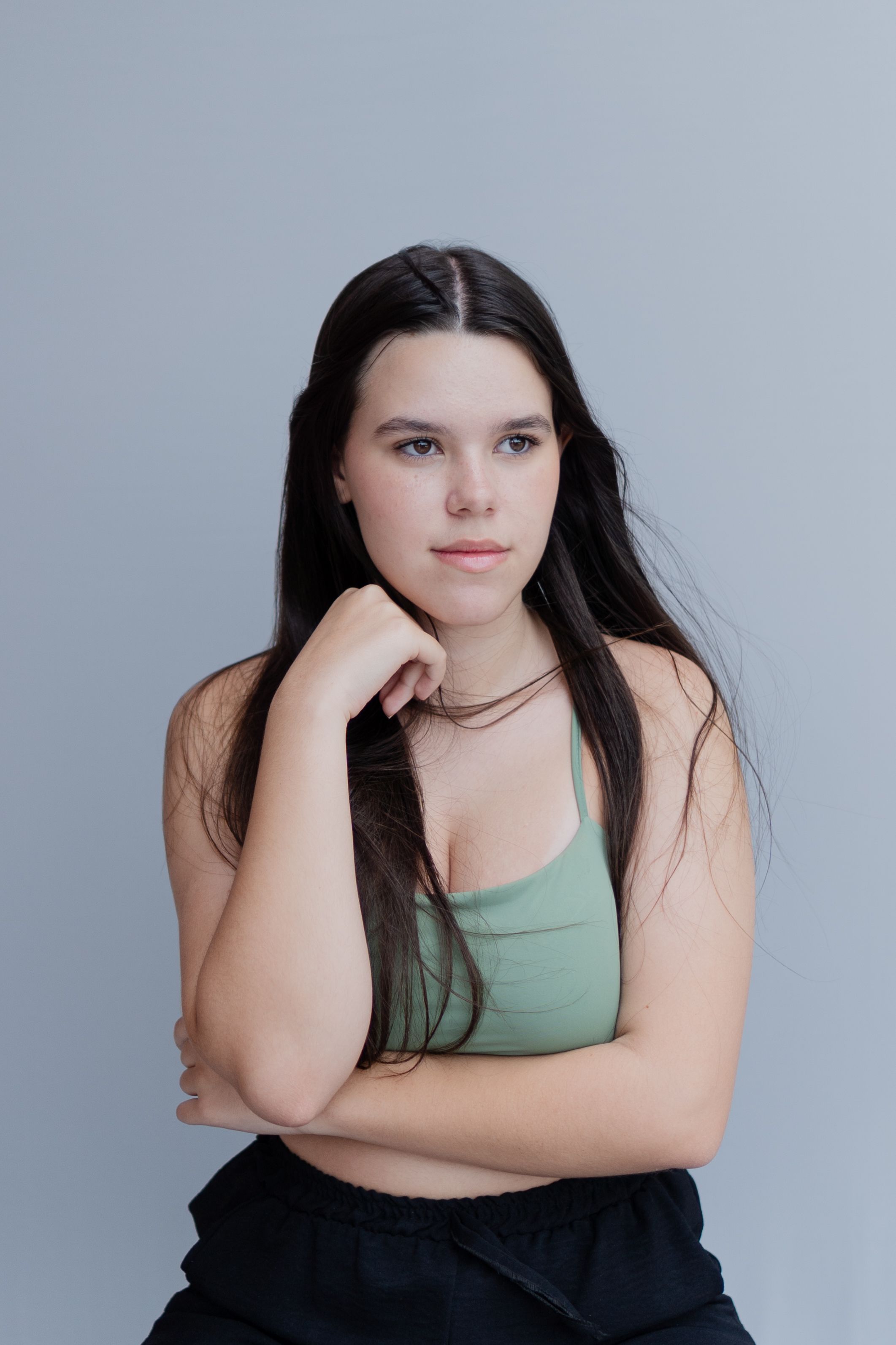 Portrait of a young woman with long dark hair and a green top against a plain background.