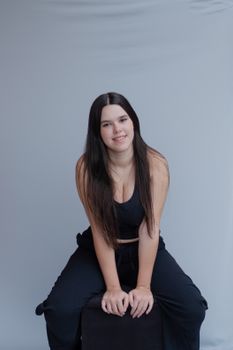 Portrait of a young woman in a relaxed pose wearing a black outfit against a simple studio backdrop.