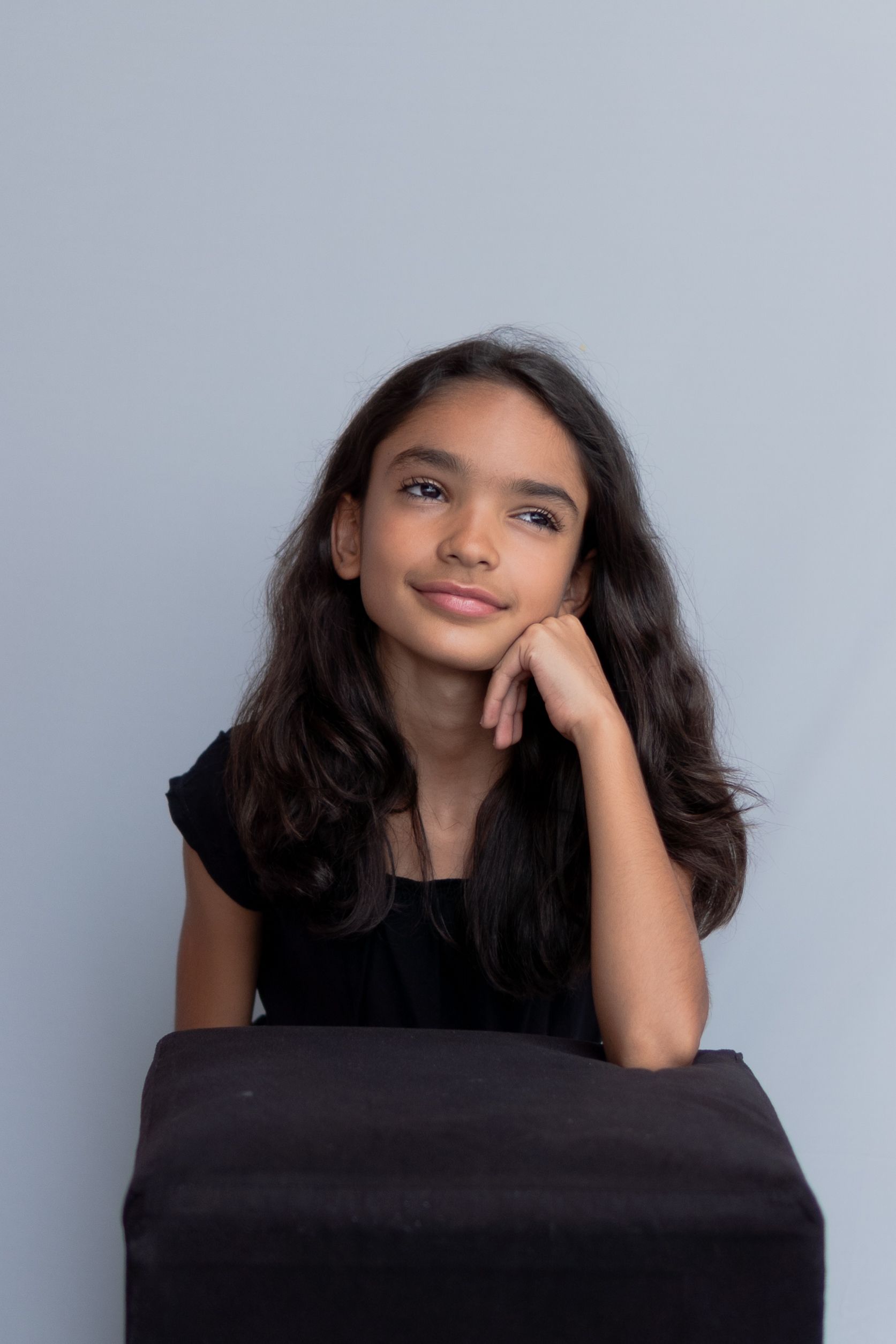 A young girl in a contemplative pose against a soft gray background, exuding calmness.