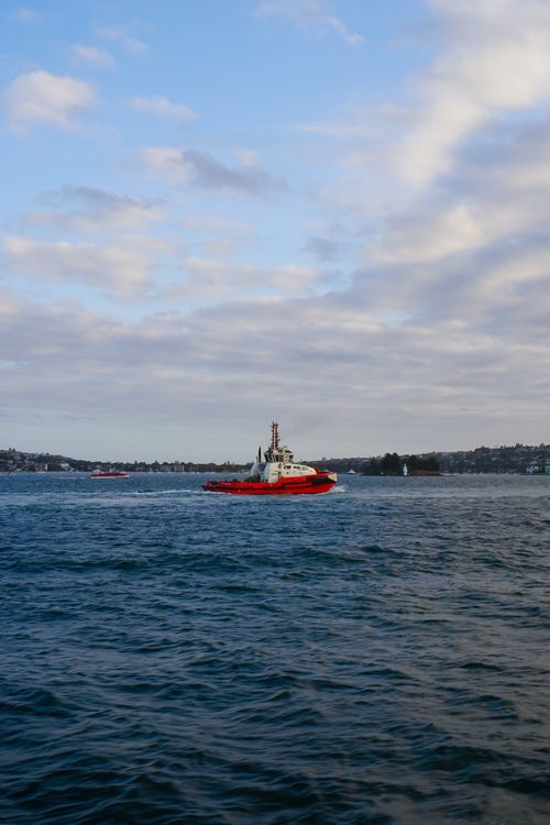 Free A red tugboat navigating the calm ocean waters, with a cloudy sky above. Stock Photo