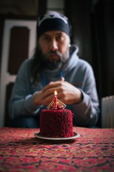 A person contemplating a single lit candle on a red velvet cake, set in an Istanbul room.