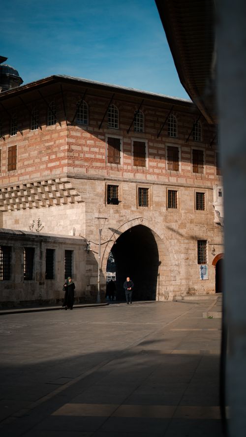 Free A historic stone building with arched entrance and people walking. Stock Photo