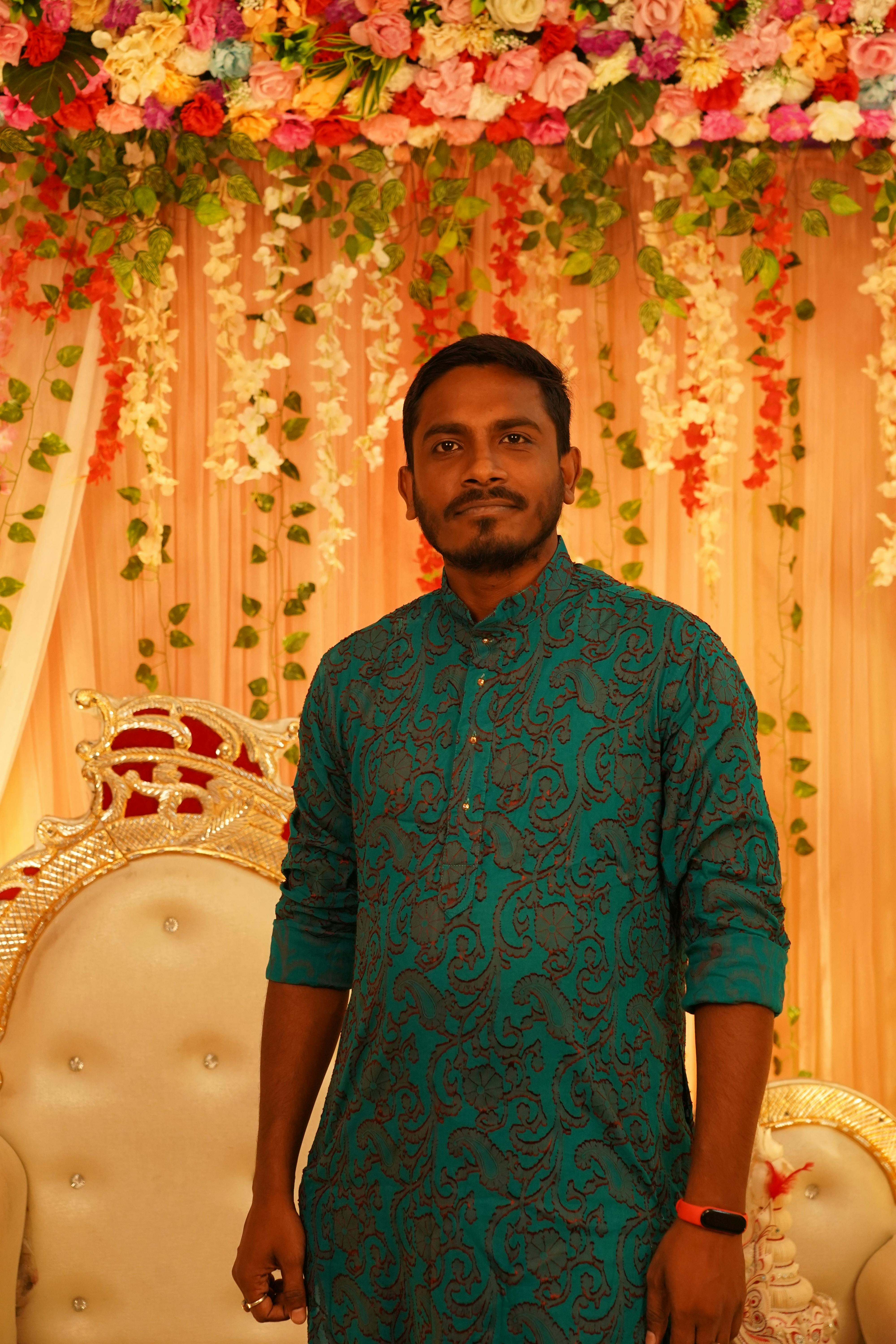 Man in traditional attire standing at a floral decorated event setting indoors.