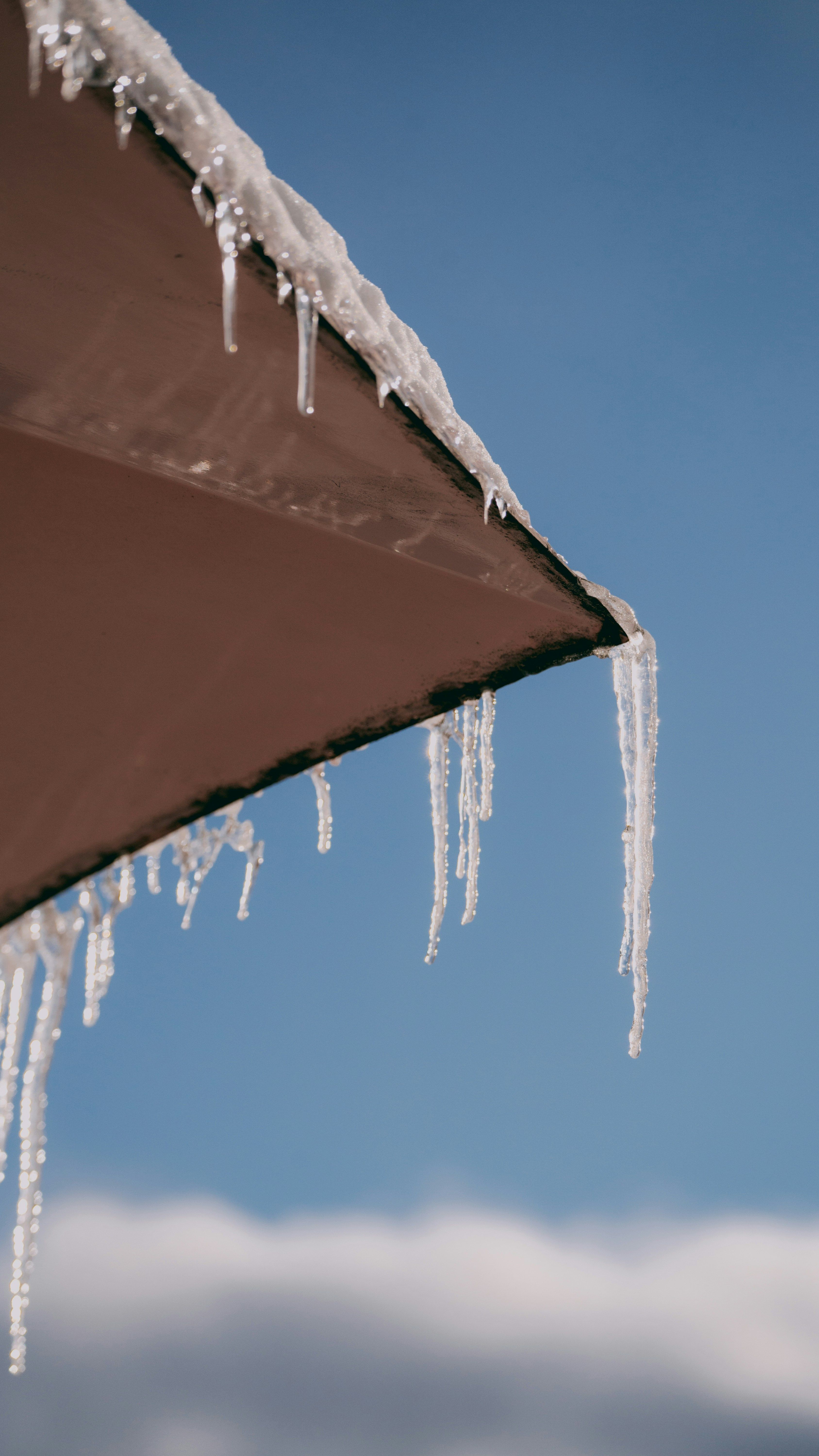 Section of aluminum gutter hanging loose from the edge of a roof