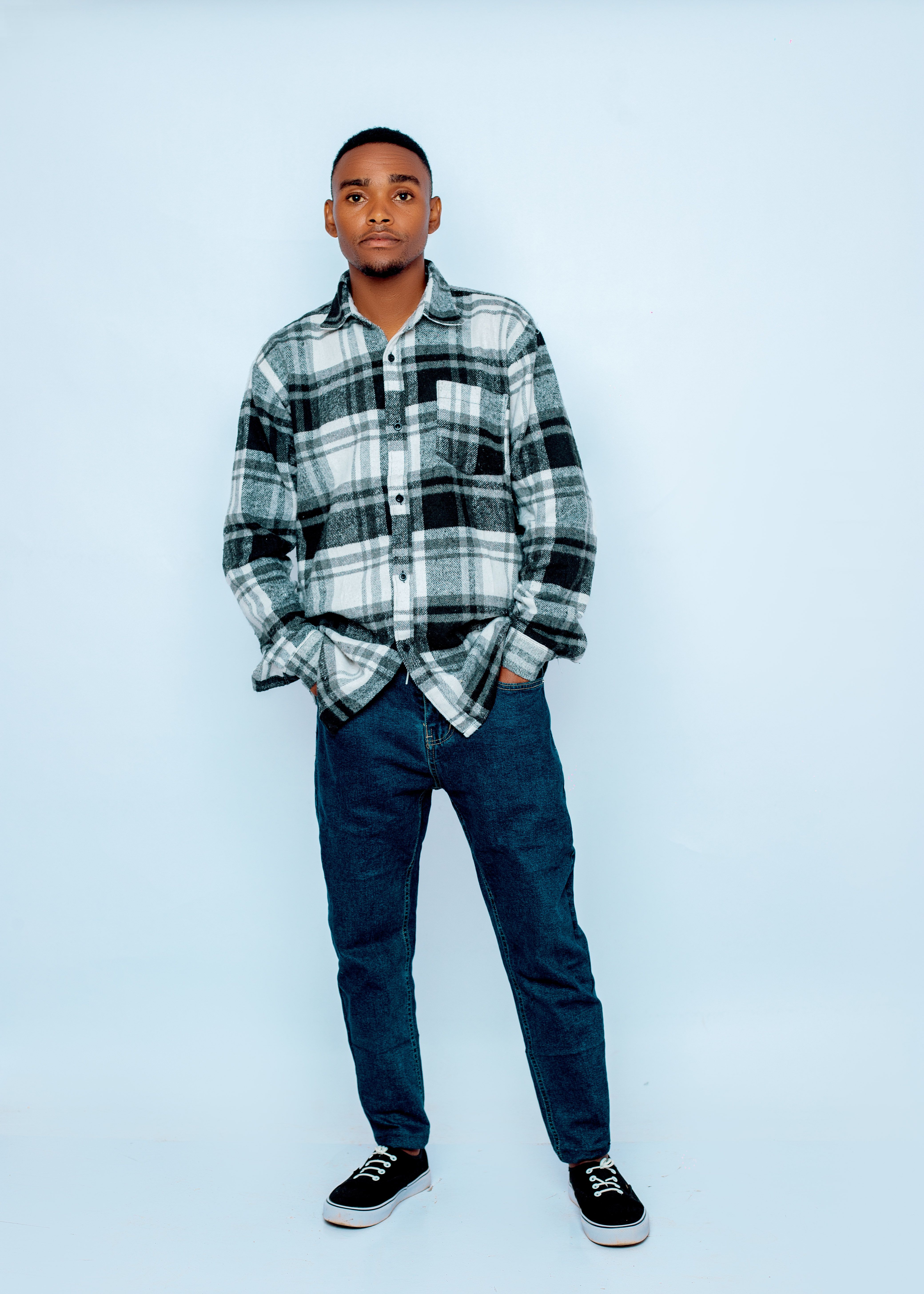 Casual portrait of young man wearing a plaid shirt and jeans, posing confidently in studio.