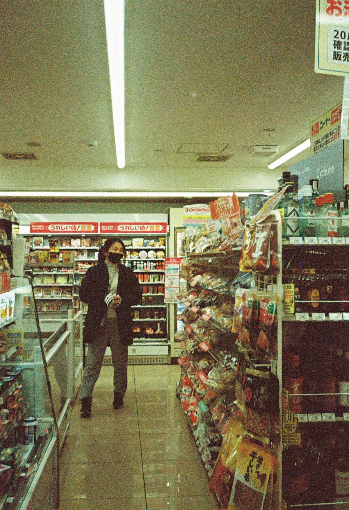 Shopper walking down a brightly lit aisle of snacks inside a Japanese convenience store