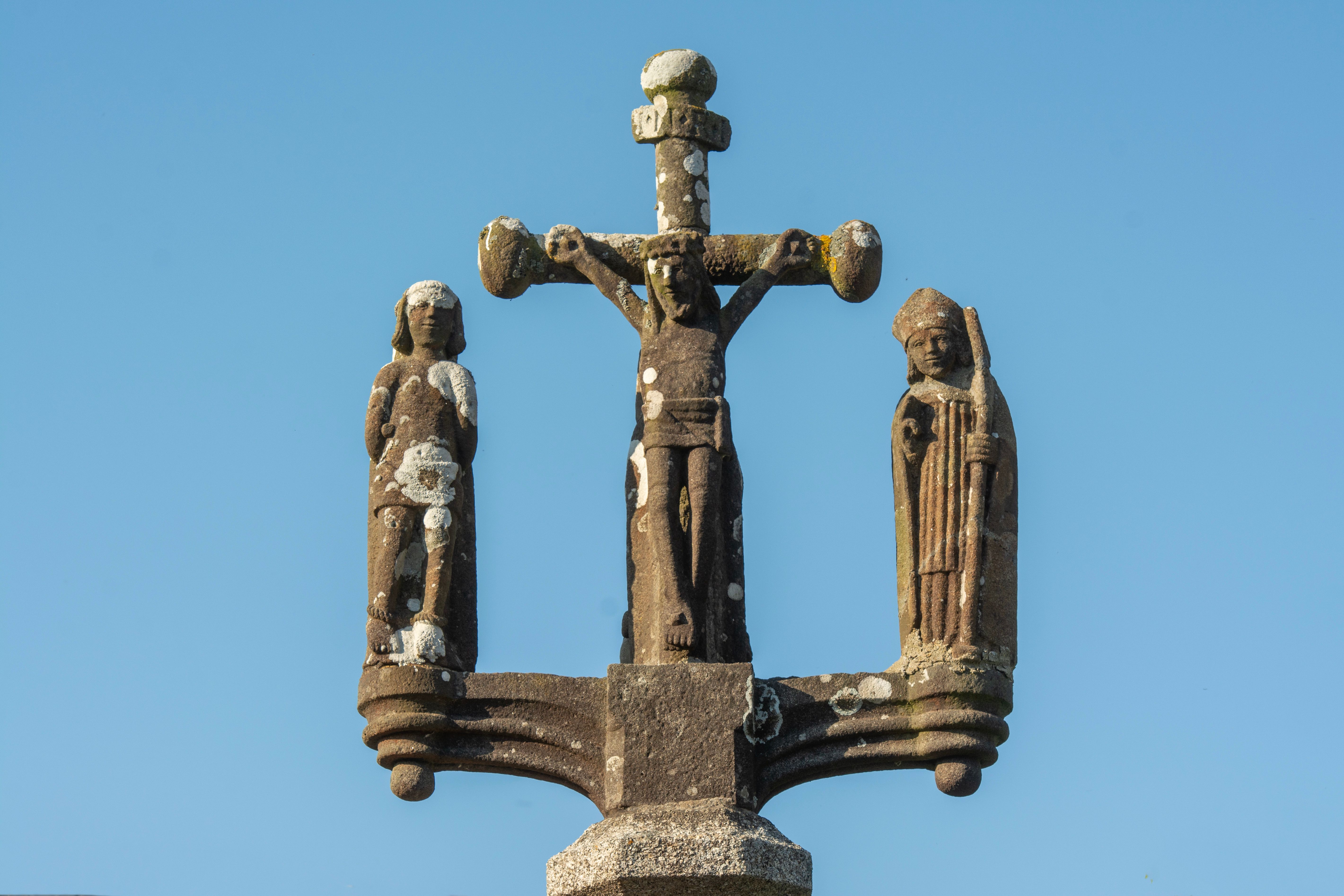 Ancient weathered stone crucifix set against a clear blue sky.