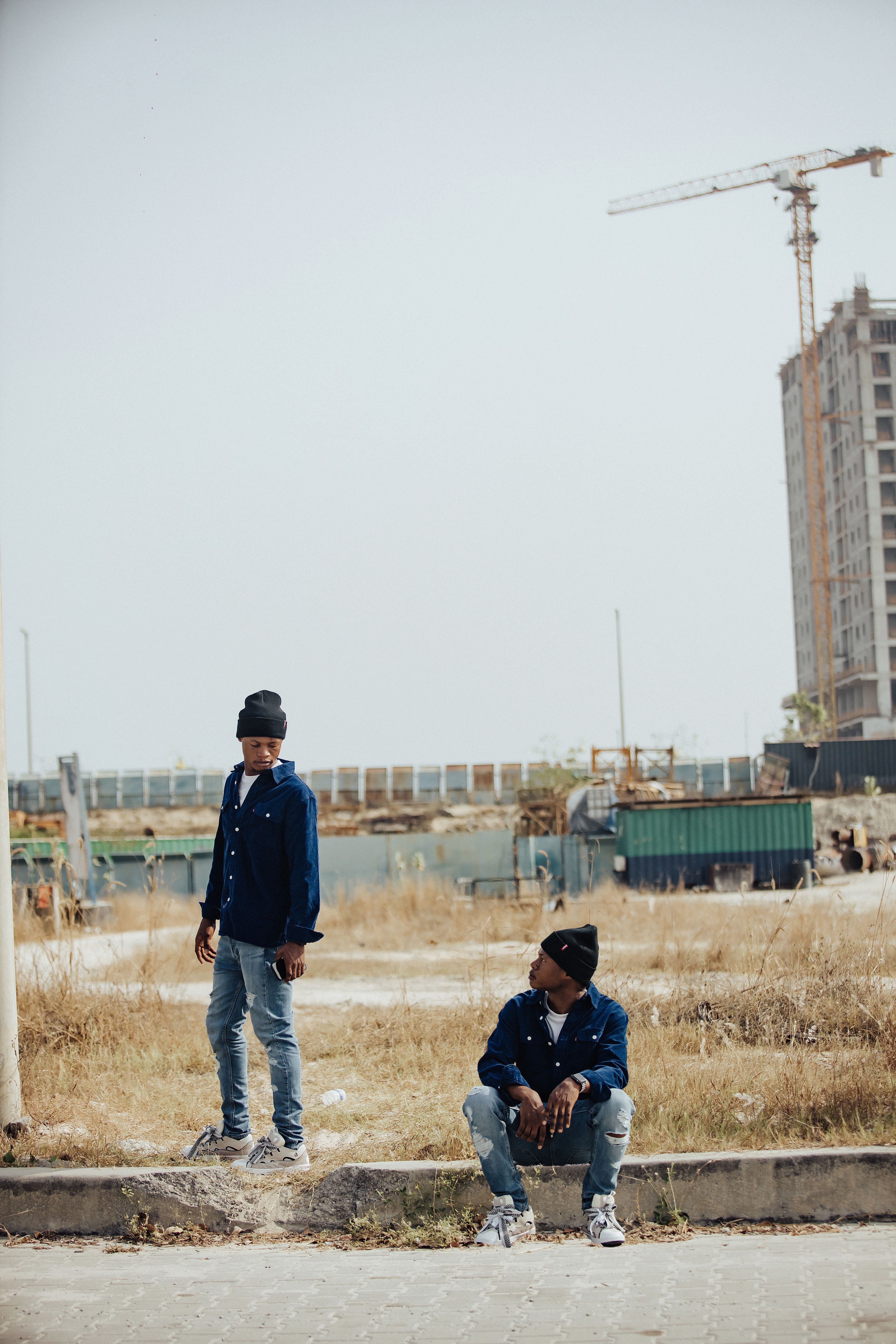 Two young men in casual attire posing in a developing urban area.