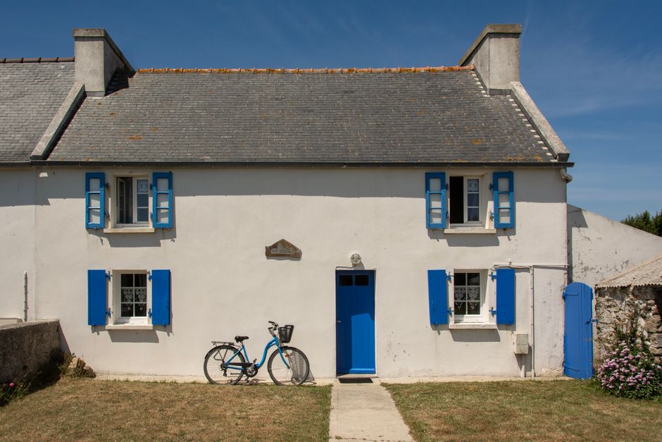 Picturesque house with blue shutters and bicycle in Ouessant, France.