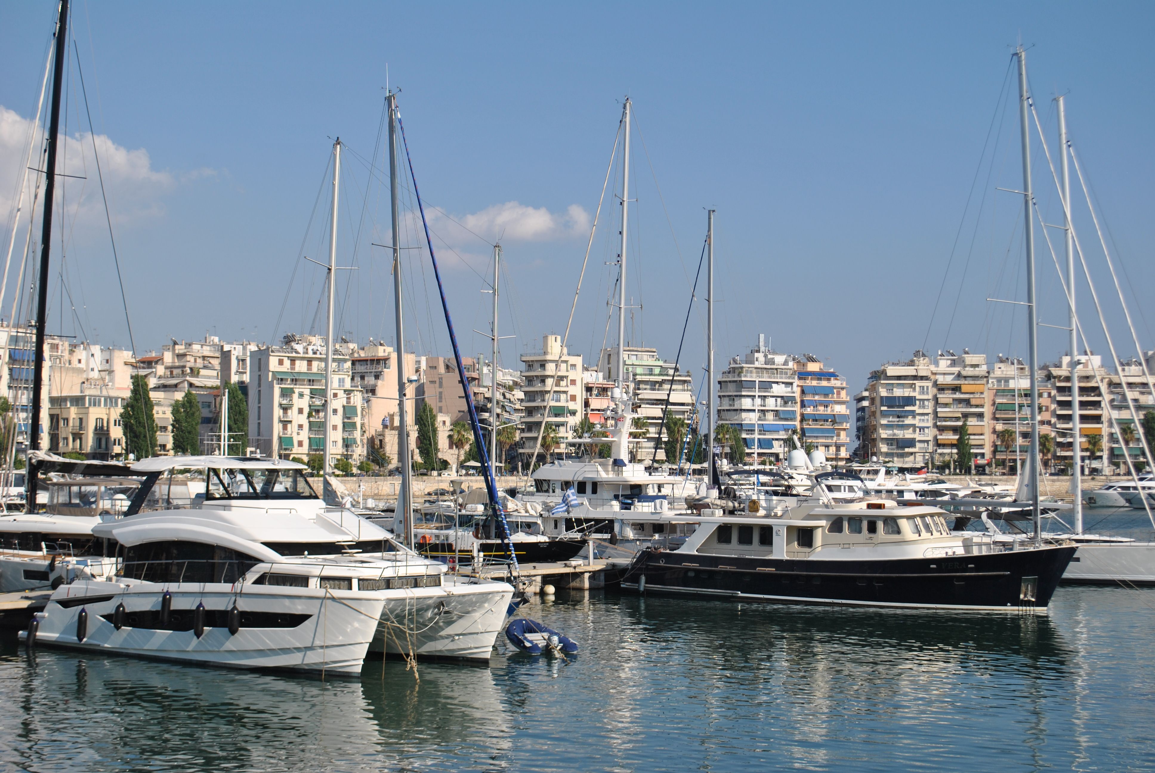 Luxury yachts docked at a city marina with modern high-rise buildings in the background.