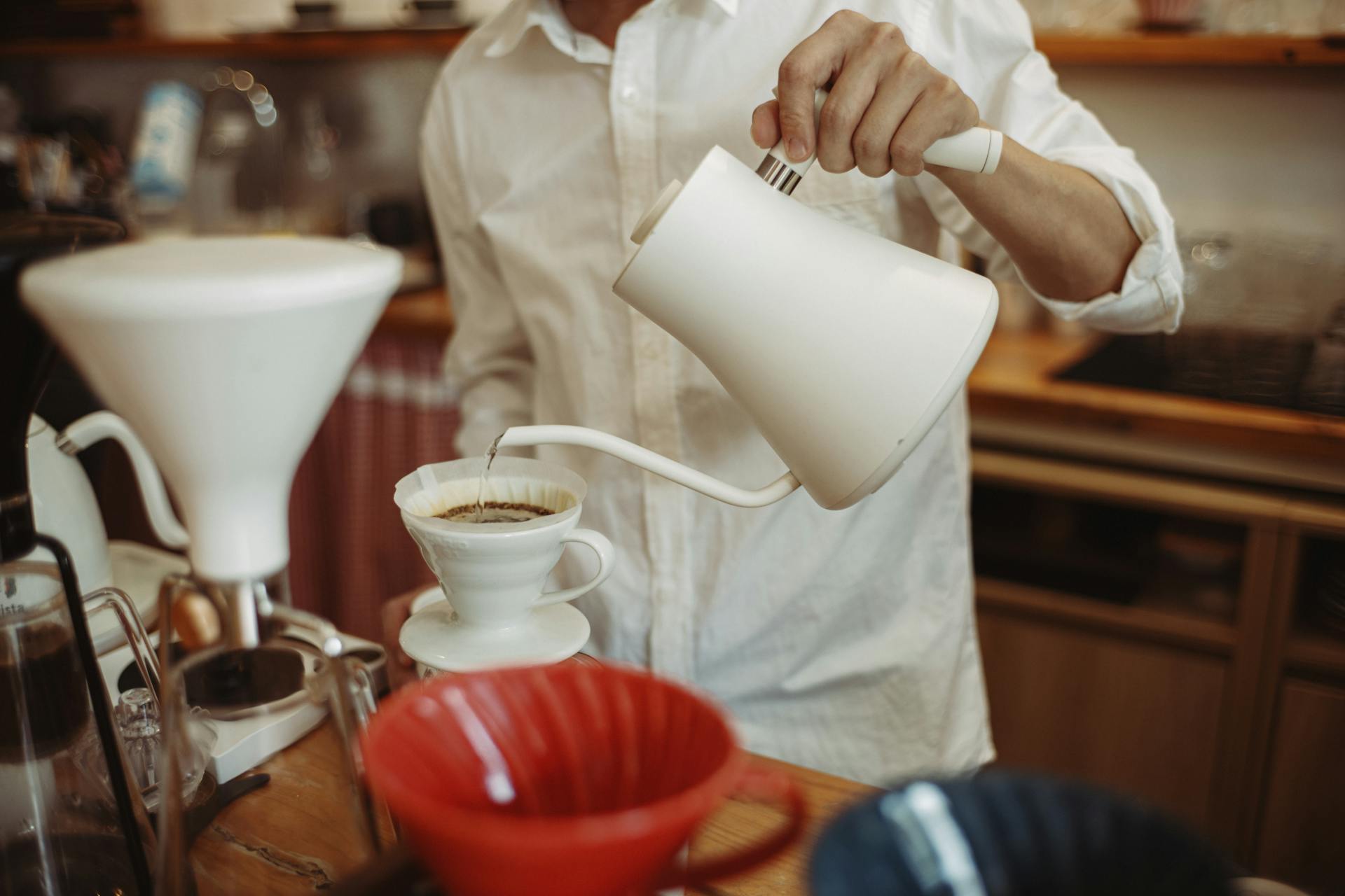 Barista expertly pouring coffee with gooseneck kettle in a cozy cafe environment.