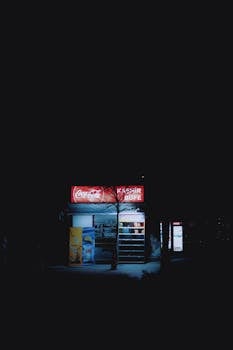 A small kiosk lit softly at night on a quiet street.