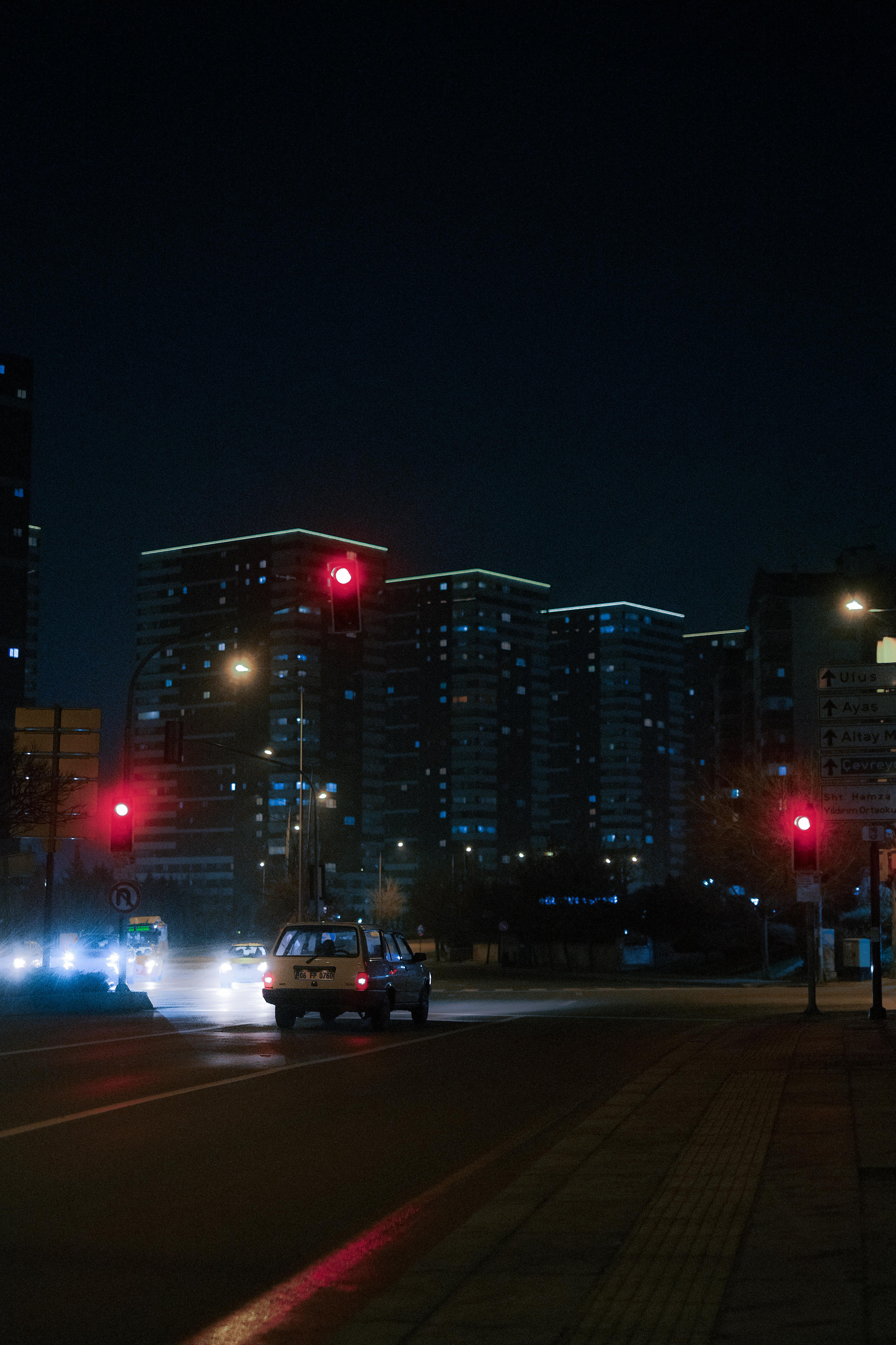 City at night with car at red traffic light. Illuminated buildings in background.