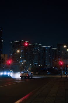 City at night with car at red traffic light. Illuminated buildings in background.