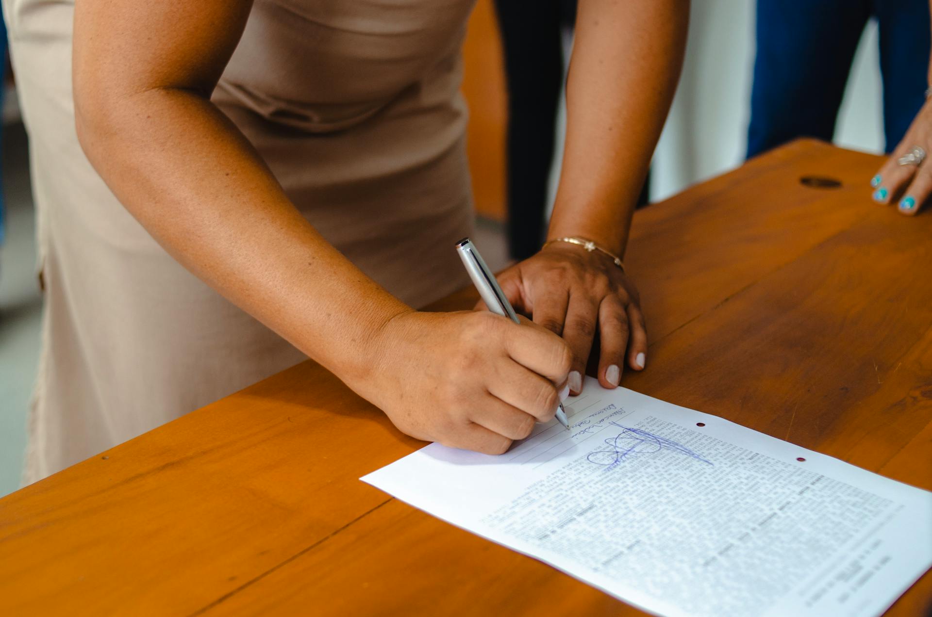 A professional woman signing an official document on a wooden table indoors.