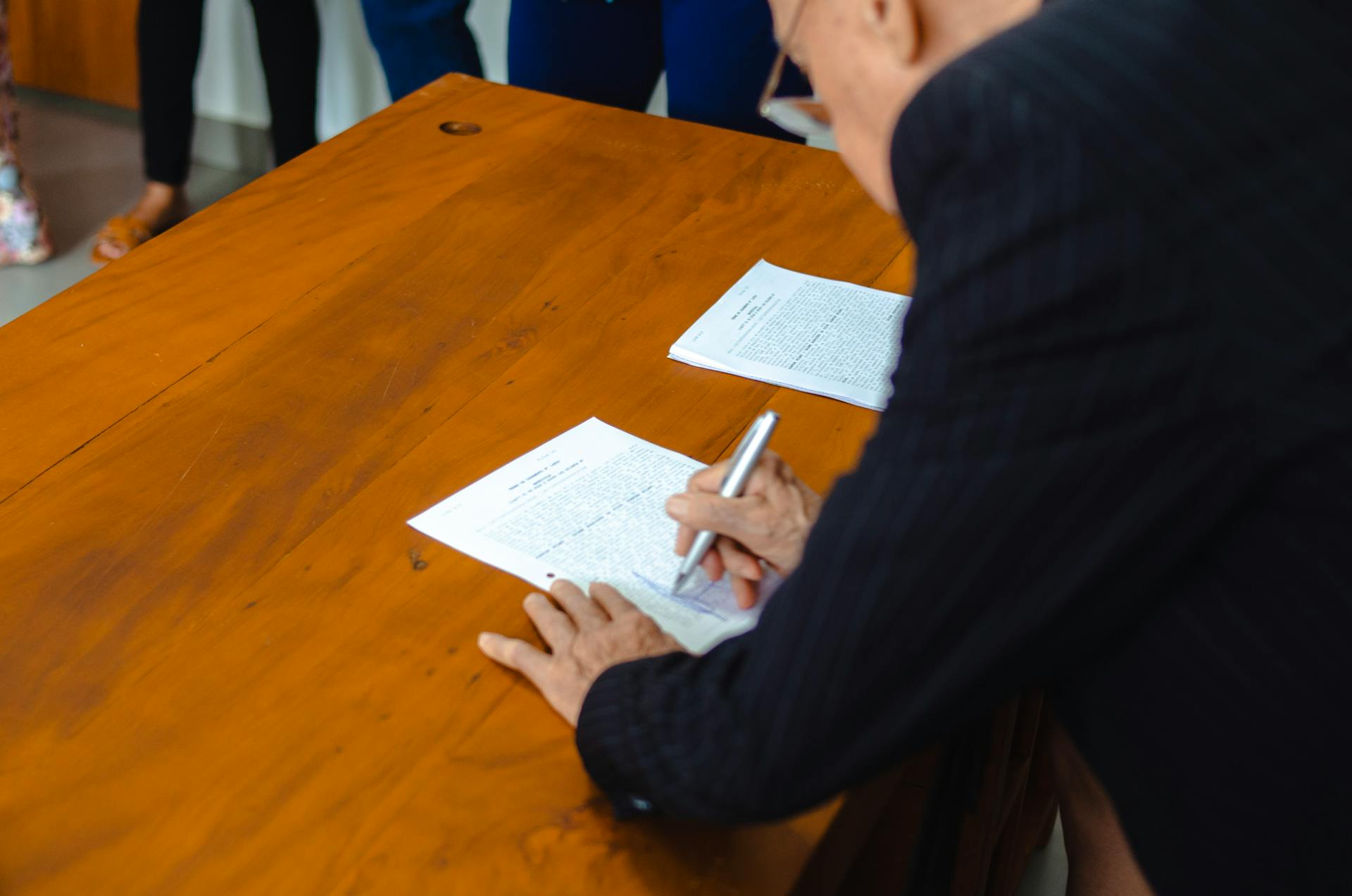 A close-up of a businessman signing official documents at a wooden desk.