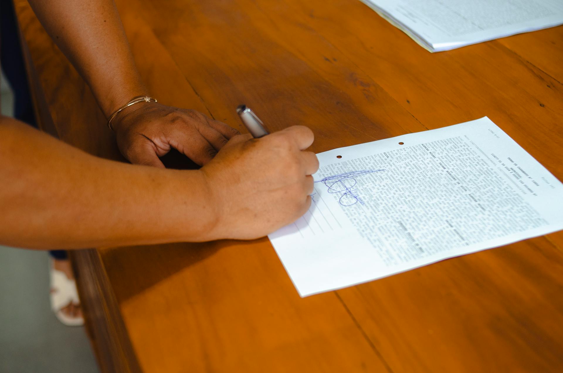 Close-up of hands signing a legal document on a wooden table indoors.